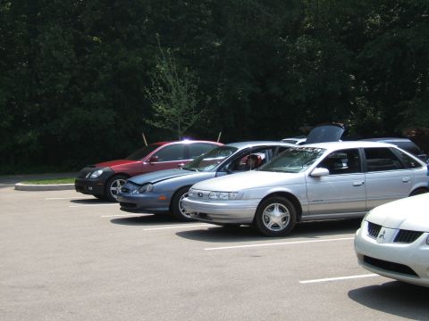 1998 Ford Taurus - A silver sedan is parked in a lot with its hood open, alongside other vehicles.