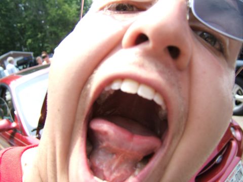 1998 Ford Taurus - A person's open mouth fills the foreground, with a red car and other people visible behind them.