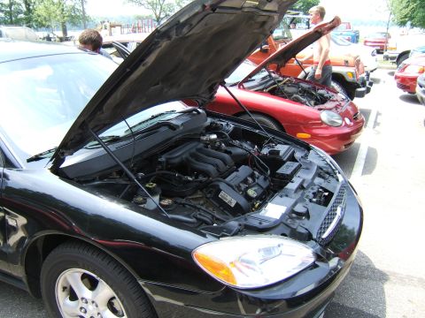 1998 Ford Taurus - A black sedan's engine is exposed to view, parked next to a red car with its hood also open.