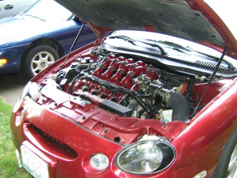 1998 Ford Taurus - Engine bay of a 1998 Ford Taurus, custom red intake runners and a blue car in the background.