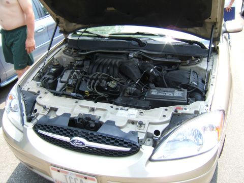 1998 Ford Taurus - The engine compartment of a gold sedan is open, revealing the engine and other components under the hood.