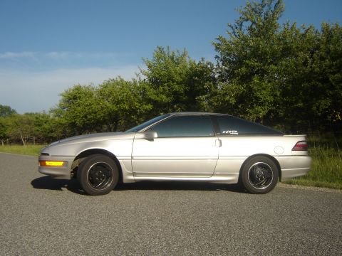 1990 Ford Probe - A silver 1990 Ford Probe coupe is parked on the side of a road with trees in the background.