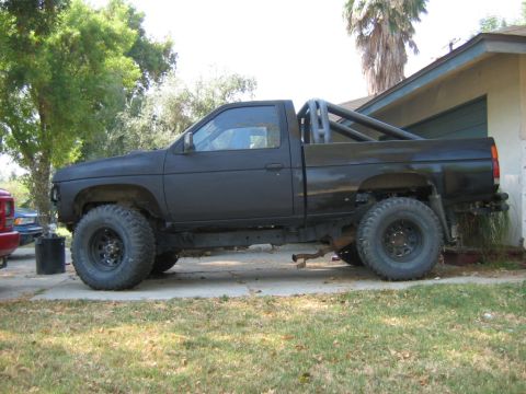 1991 Nissan Pathfinder - This modified black pickup truck, likely from the mid-1990s, sits on a driveway with a house and trees in the background.