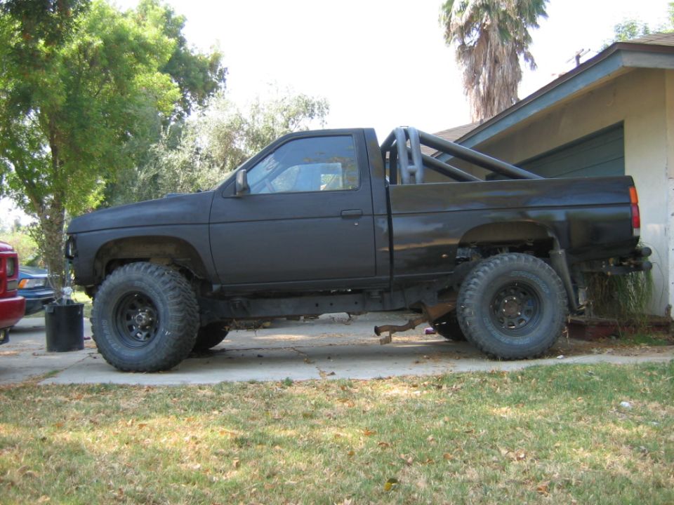 Black pickup truck with lifted suspension and roll bar, parked on a driveway