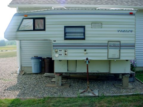 1973 Ford Ranchero - A white truck camper, identified by the 'VIKING' label, is parked next to a house and supported by jacks.