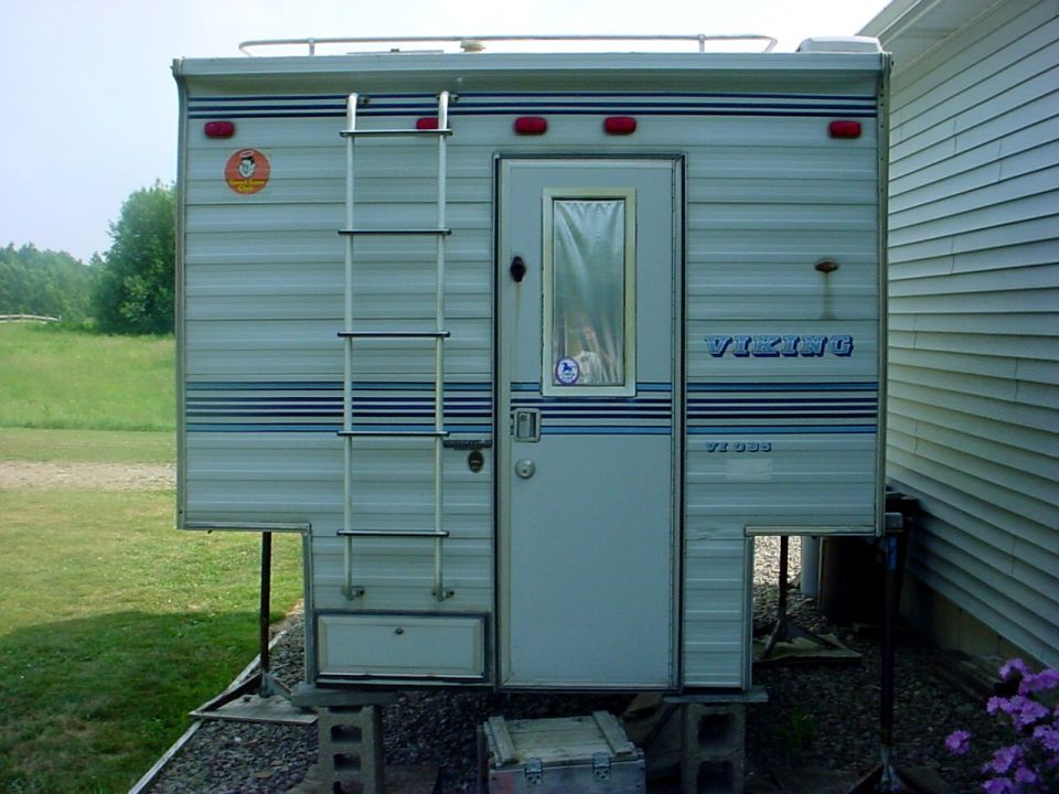 Viking truck camper mounted on blocks next to a house. Ladder on the side