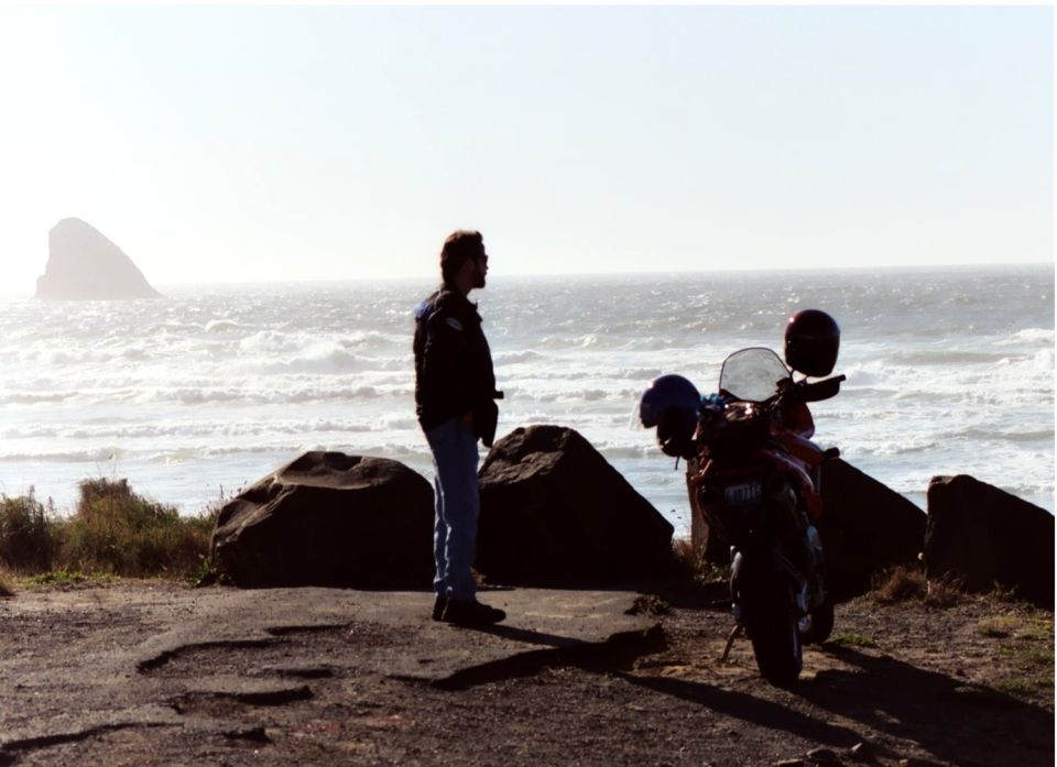 Silhouetted dual-sport motorcycle with helmet parked at a windswept ocean overlook