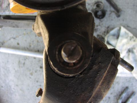 1979 Ford Bronco - Close-up of a greasy, rust-scaled steering knuckle removed from a solid front axle, with the ball-joint bore and its tapered stud and nut v…