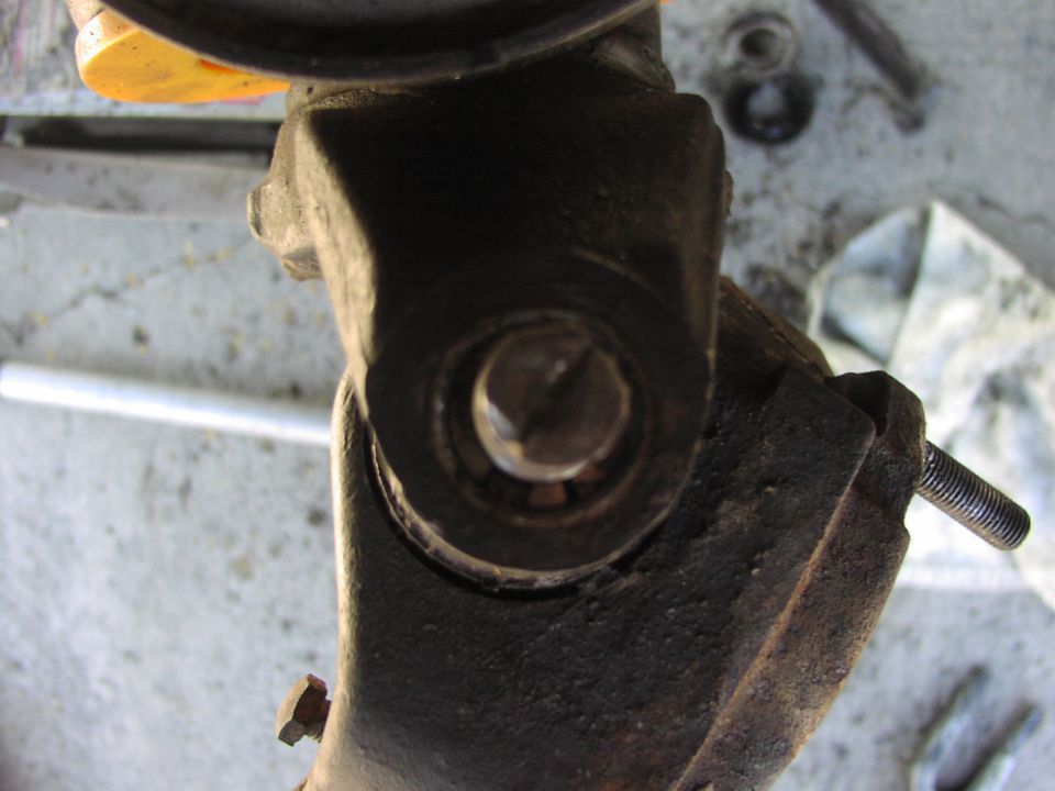Rusty steering knuckle with exposed ball joint stud and bore on a concrete garage floor