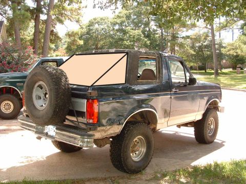 1993 Ford Bronco - A dark green Ford Bronco is parked in a driveway with a spare tire mounted on the rear.