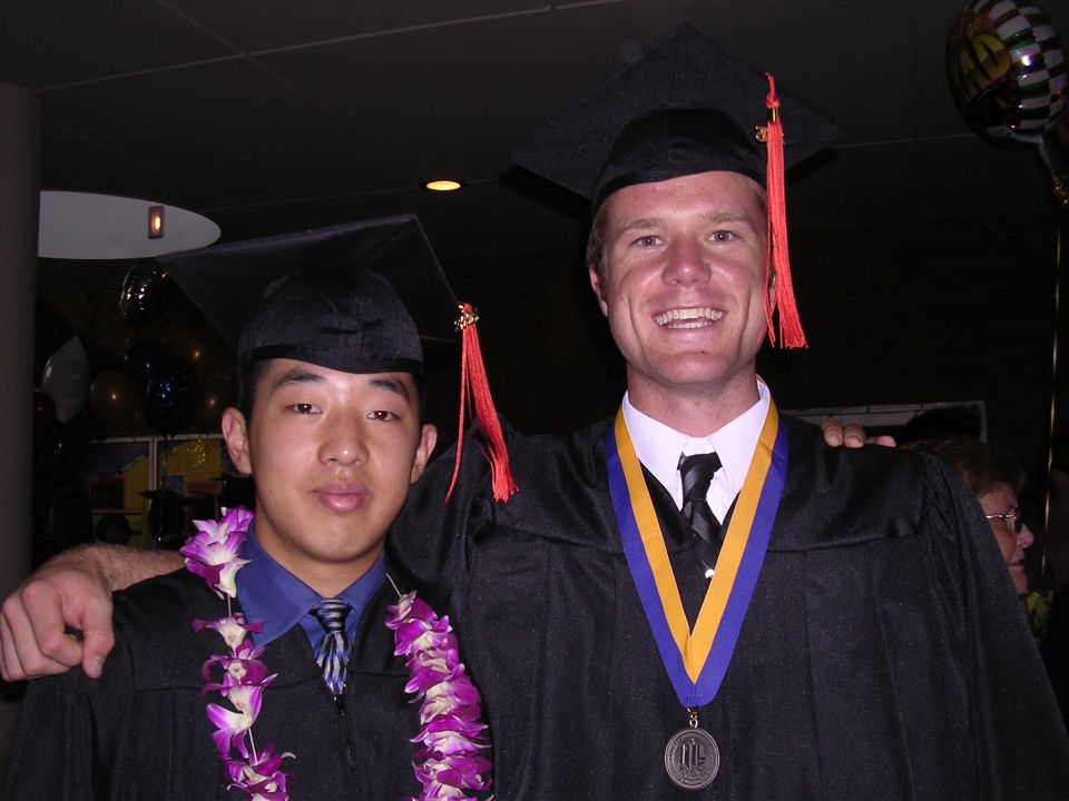 Two young men in graduation caps and gowns, one wearing a lei