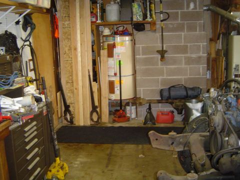 1989 Ford Bronco - A cluttered garage contains a water heater, tools, and the front end of a disassembled vehicle.