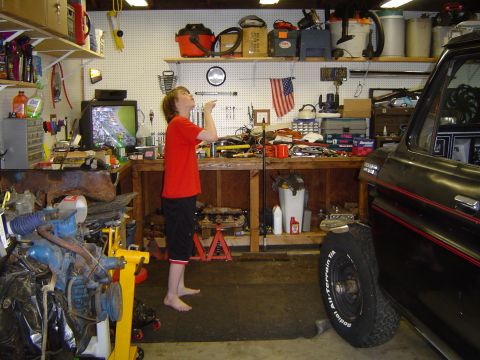 1989 Ford Bronco - A black Ford Bronco is parked in a cluttered garage with a person looking up.