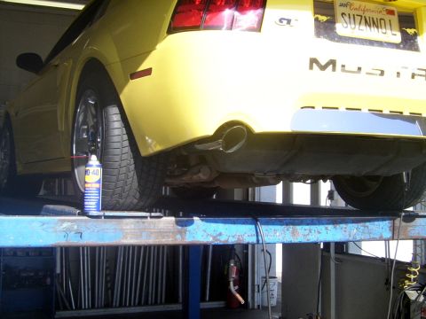 2002 Ford Mustang - Rear view of a yellow 2002 Ford Mustang GT on a lift, showing the exhaust and a WD-40 can.