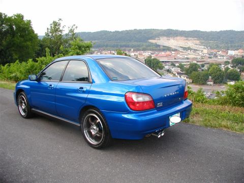 2002 Subaru Impreza - A blue Subaru Impreza WRX is parked on a roadside overlooking a town and a bridge.