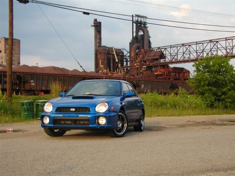 2002 Subaru Impreza - A blue Subaru Impreza is parked in front of an industrial complex with train cars.