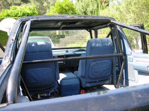 1985 Ford Bronco - Interior view of a modified SUV, showing blue seats and a roll cage, with another vehicle in the background.
