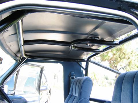 1985 Ford Bronco - The interior of a vehicle is shown, a prominent roll cage and blue upholstered seats.