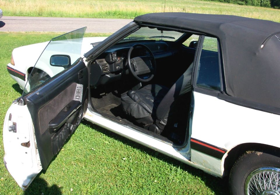 Open driver door of white Fox-body convertible showing gray interior and dashboard