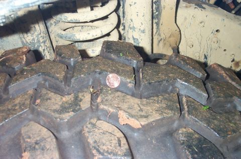 1987 Ford Bronco - Close-up of a dirty tire tread with a penny for scale, showing part of the vehicle's suspension.