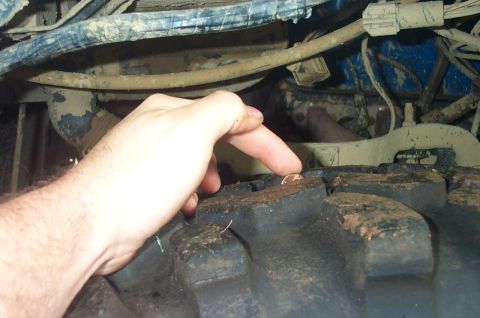 1987 Ford Bronco - A finger points to an object stuck in the tread of a large off-road tire. The SuperMotors logo is visible in the lower right corner.