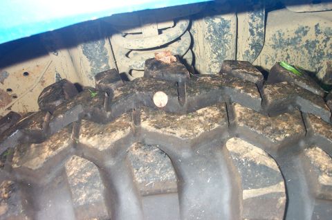 1987 Ford Bronco - A nail is stuck in the tread of a dirty off-road tire, with suspension components visible overhead.