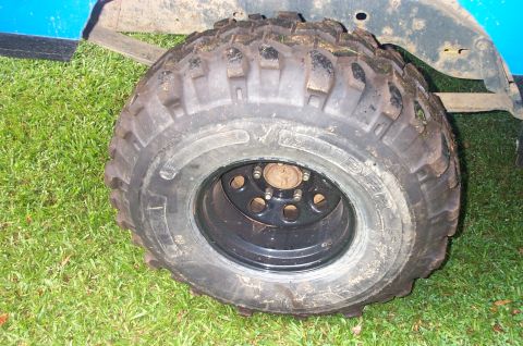 1987 Ford Bronco - Close-up of a large, knobby off-road tire mounted on a blue vehicle, with a portion of the fender visible.