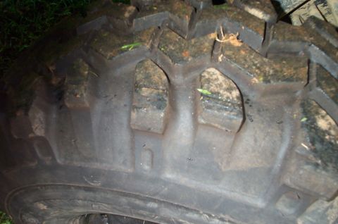 1987 Ford Bronco - A close-up view of a tire tread, showing the aggressive pattern and some mud. The SuperMotors logo is visible in the lower right corner.