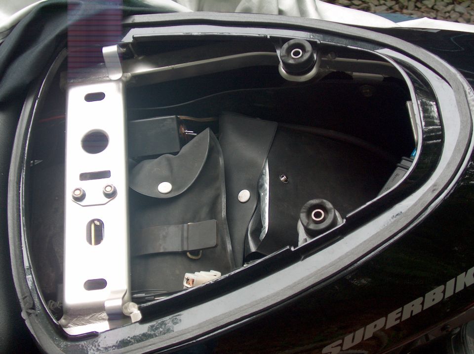 Motorcycle tail section open, showing black storage compartment with a metal bracket and a folded black pouch inside