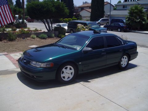 1993 Ford Taurus - A green sedan with white wheels is parked in a driveway on a sunny day.