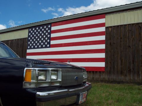 2001 Ford Crown Victoria - A dark blue sedan is parked in front of a building adorned with a large American flag mural.
