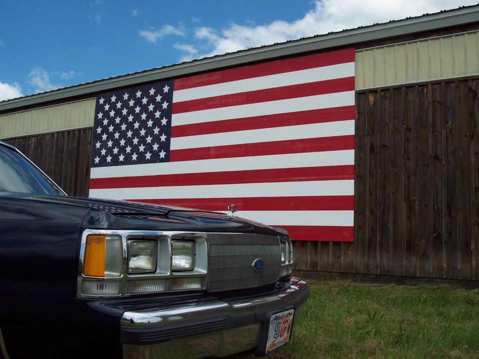 Front view of a dark blue sedan parked in front of a large American flag mural