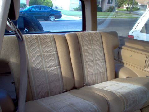 1985 Ford Bronco II - Interior view of a 1985 Ford Bronco II, with rear seats and a spare tire visible. Another car is parked outside.