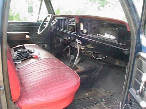 1977 Ford F-250 - The interior of a 1977 Ford F-250 shows a red bench seat and a dark dashboard with manual transmission.