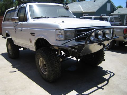 1990 Ford Bronco - White lifted Ford Bronco with a tube front bumper, off-road lights and mud-terrain tires parked on a concrete driveway.