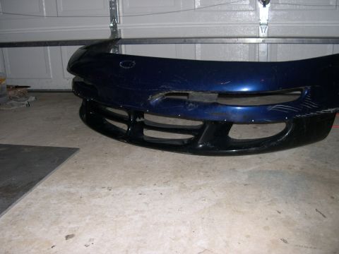 1997 Ford Probe - A detached blue car bumper with a black lower grille is shown in a garage setting.