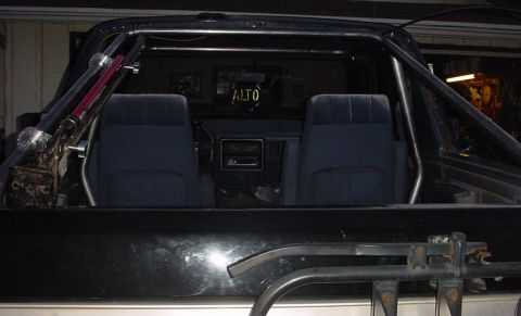 1988 Ford Bronco - The interior of a vehicle is visible, a prominent roll cage and dark blue seats. Text reading 'ALTO' is visible on the rear window.