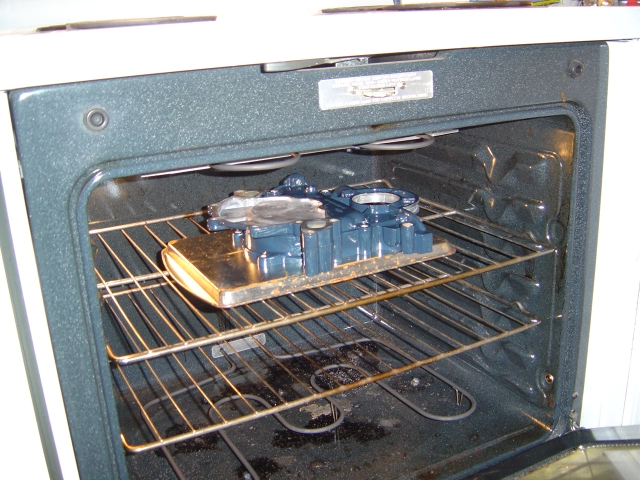Blue-painted timing cover and water pump curing on a tray inside a kitchen oven