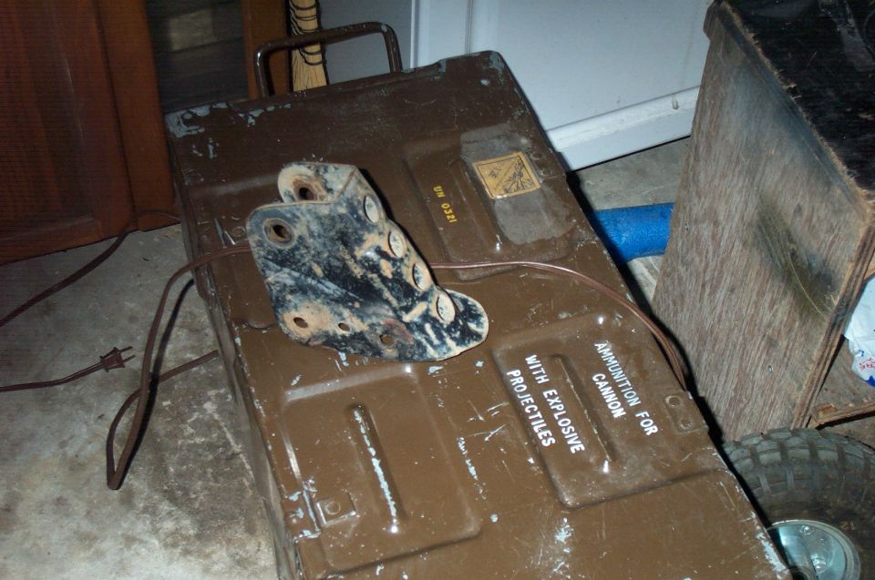 Olive-drab military ammo can with cannon ammunition stenciling on concrete floor.