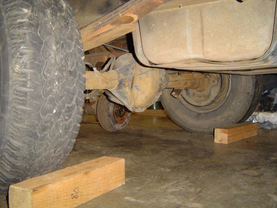 Underbody view of a truck on wooden blocks showing axle, leaf spring and fuel tank
