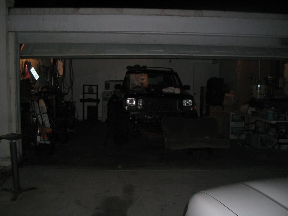 Dark Jeep Cherokee parked nose-out in a dim garage mid-project with removed seat beside it