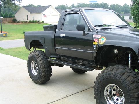 1986 Ford F-150 - This heavily modified black pickup truck features large off-road tires and custom side steps, suggesting it's built for terrain.