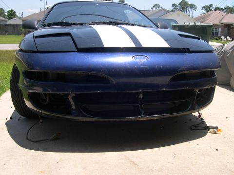 1997 Ford Probe - The front of a blue car with racing stripes is shown with its bumper removed, revealing exposed wiring.