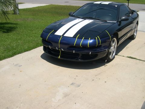 1997 Ford Probe - A blue 1997 Ford Probe with racing stripes is parked on a concrete driveway, with yellow tape on its front bumper.