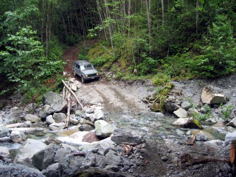 2000 Jeep Cherokee - Jeep Cherokee navigates a challenging off-road trail through a wooded area with a stream.