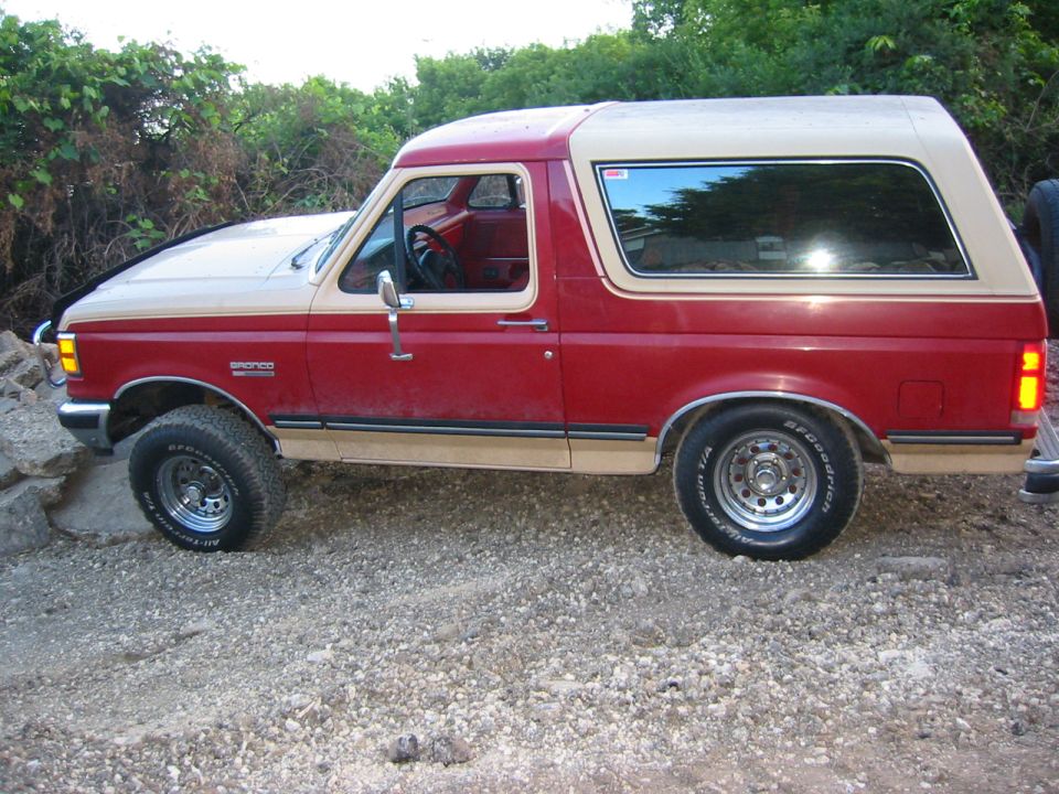 Red and tan two-door Ford Bronco SUV in side profile on gravel terrain