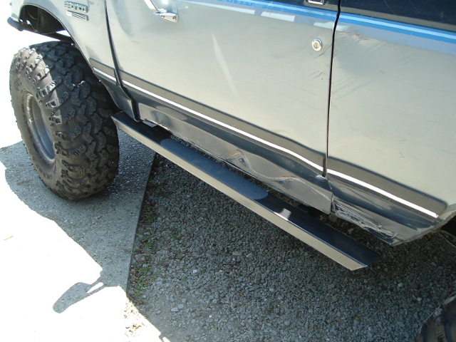 Close-up of truck rocker panel and tube step over chunky mud tire on gravel