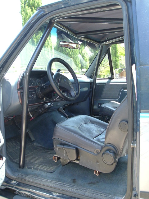 1989 Ford Bronco - The interior of a dark blue SUV is visible, a roll cage and leather seats.
