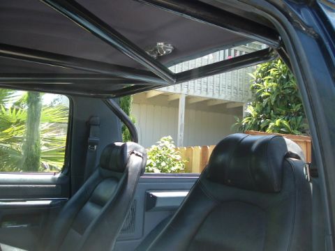 1989 Ford Bronco - The interior of a vehicle is shown, black leather seats and a prominent roll cage structure above.