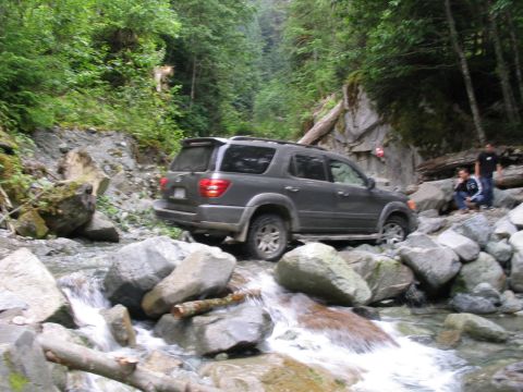 2000 Jeep Cherokee - SUV driving through a rocky stream in a wooded area.